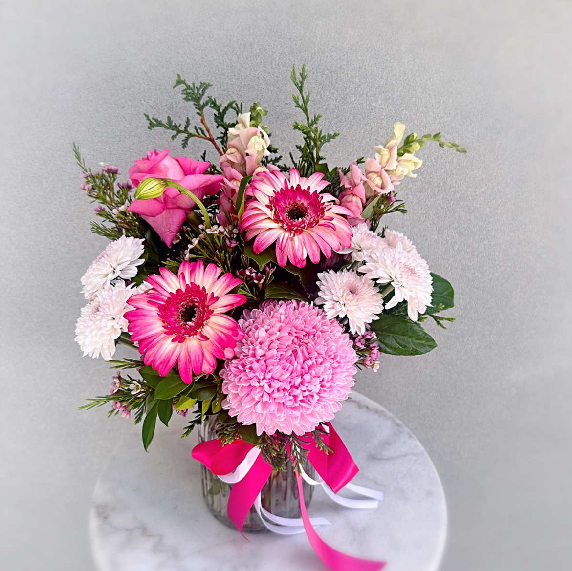 Bouquet arrangement of pink and white flowers featuring gerberas, roses and chrysanthemums in a clear vase with ribbon
