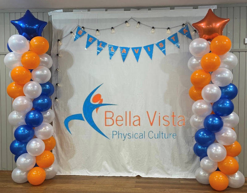 Decorative setup with balloons and a banner for Bella Vista Physical Culture event.