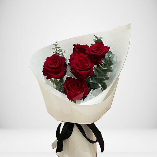 Bouquet of red roses wrapped in white paper with a black ribbon on a light gray background