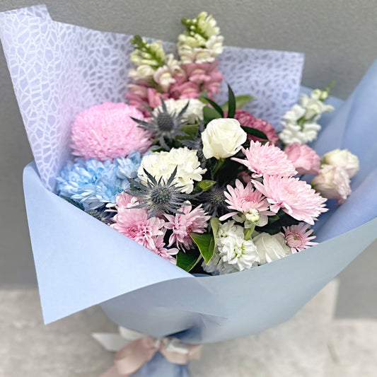 Bouquet of pastel pink and blue flowers wrapped in light blue paper against a neutral background