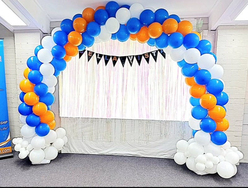 Balloon arch with blue, orange, and white balloons in front of a draped stage.