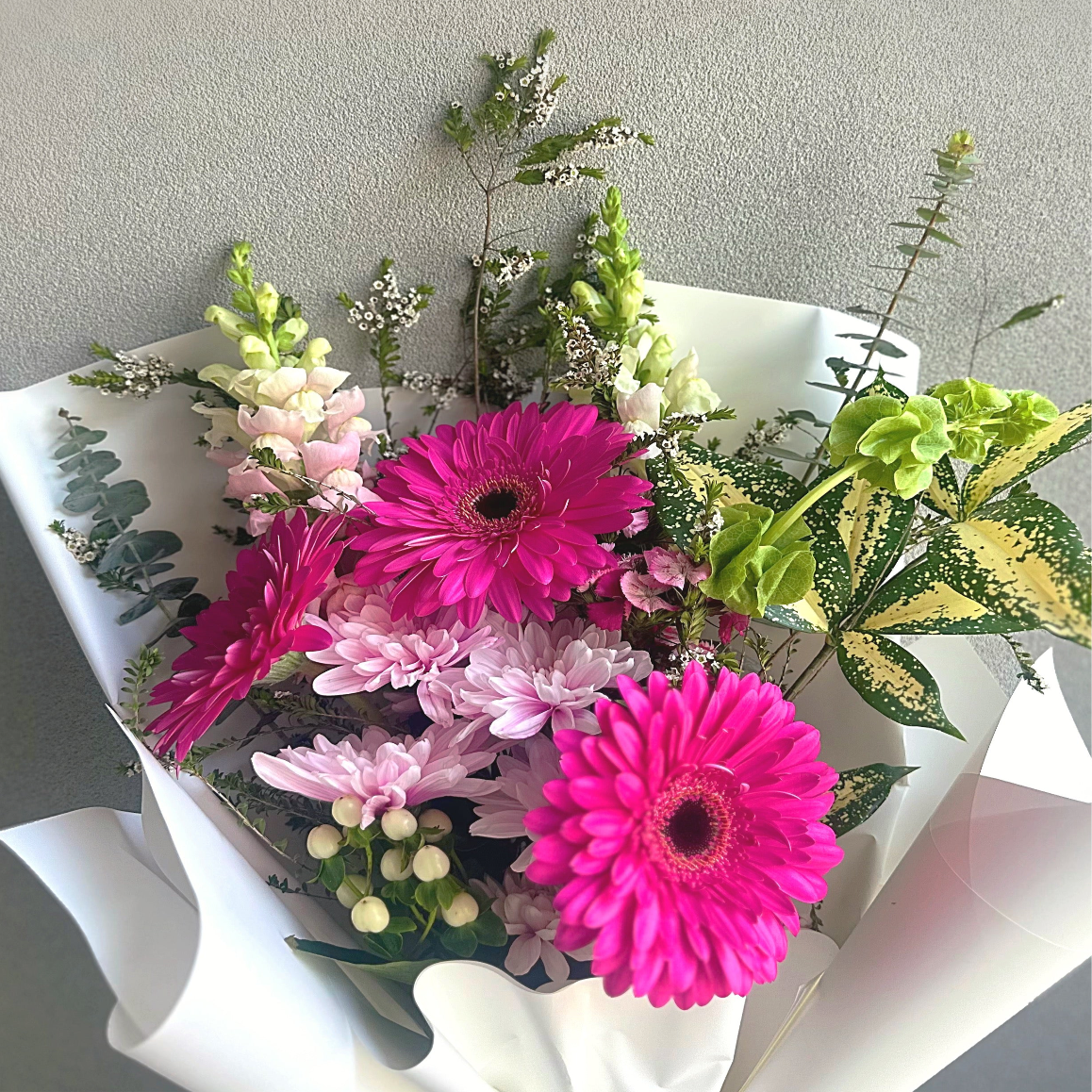 Bouquet of pink and green flowers with white paper wrap on a neutral background